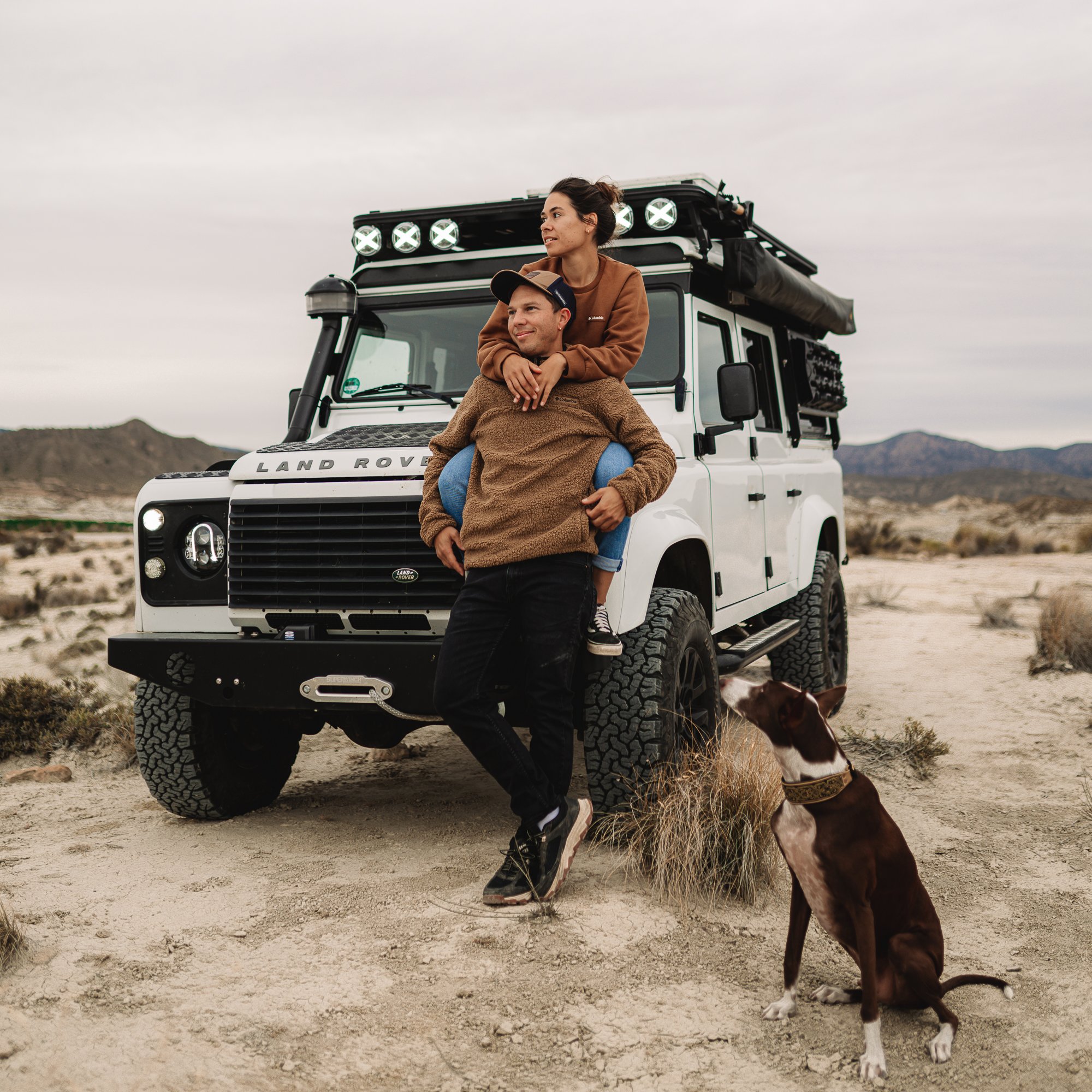 Ein junges Paar, welches auf einem Land Rover Defender sitzt