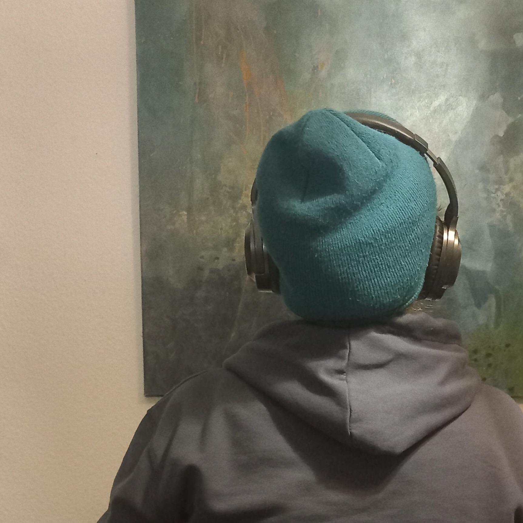 Person mit Hoody, Mütze und Kopfhörern  schaut auf ein Gemälde